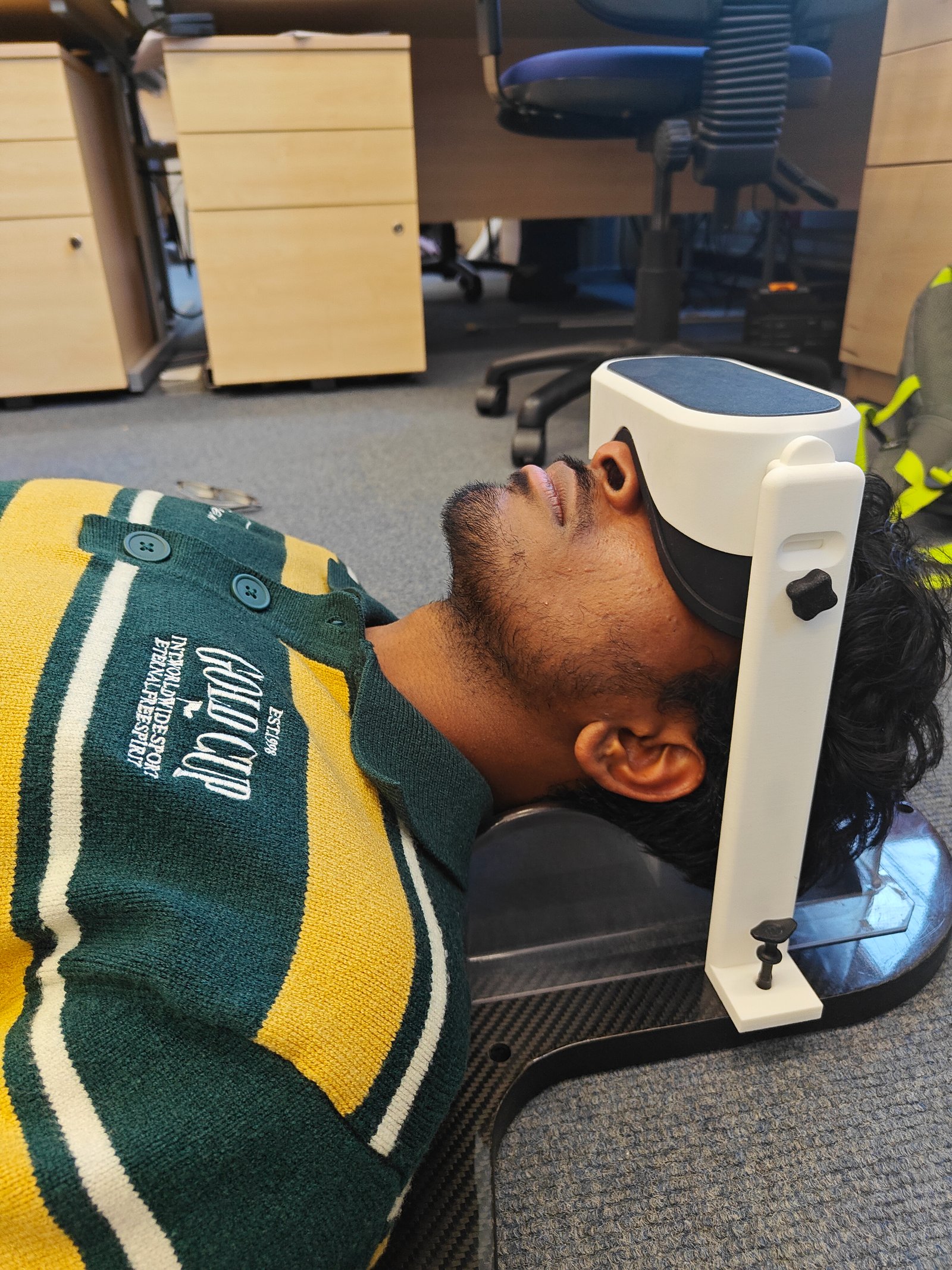 A user lying under the open IRIS VR headset mounted on its floating-arm stand
